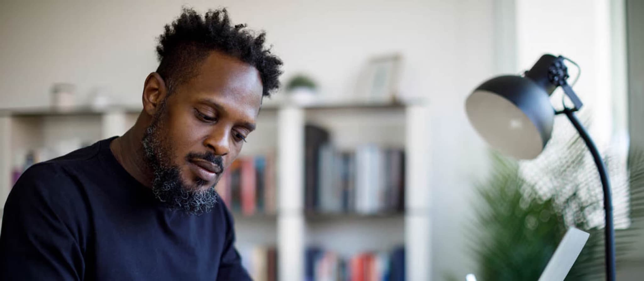 A man with a beard working at a desk with a laptop, reflecting on personal savings goals.