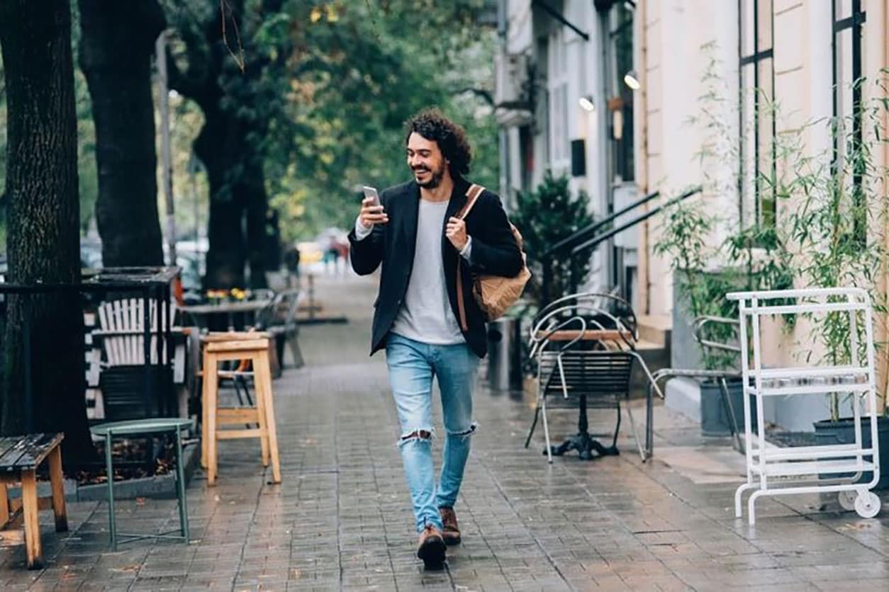 A man strolls down a street, enjoying his day while checking his credit score update on his phone.