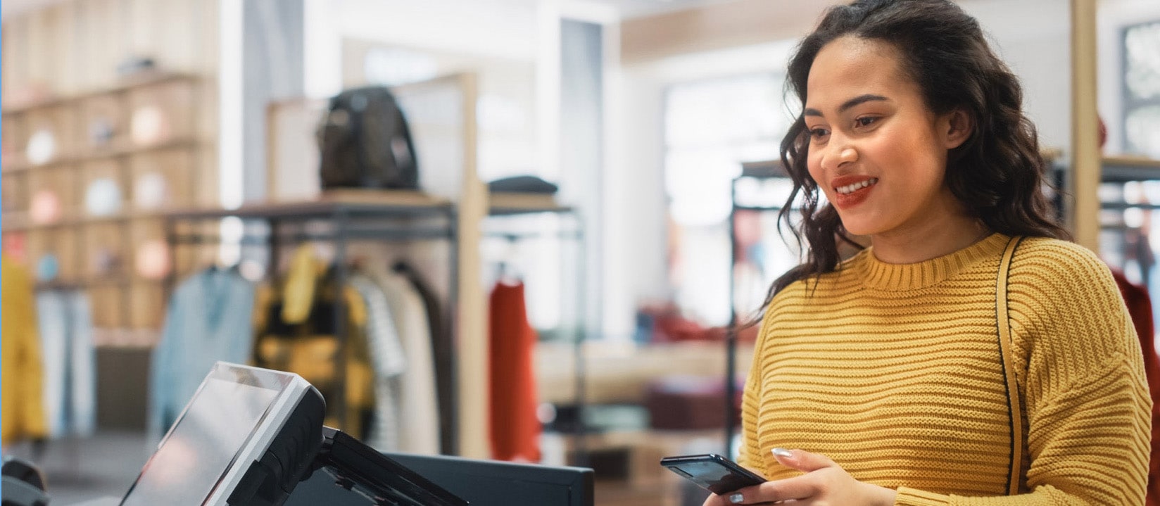 A women smiling and making a payment at a retail counter with her smartphone.