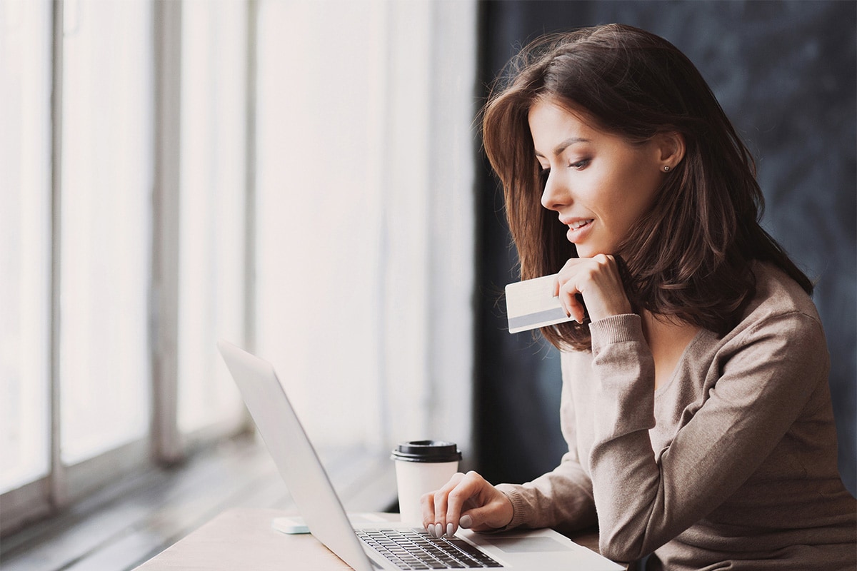 Someone holding their credit card while sitting at a desk using their laptop