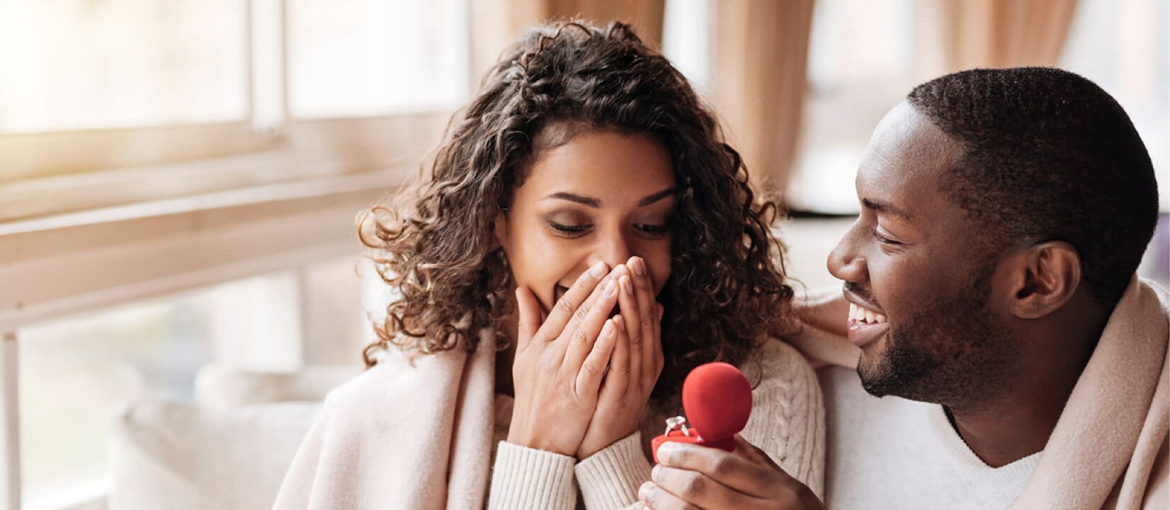 A man proposes to a woman while surprising her with an engagement ring