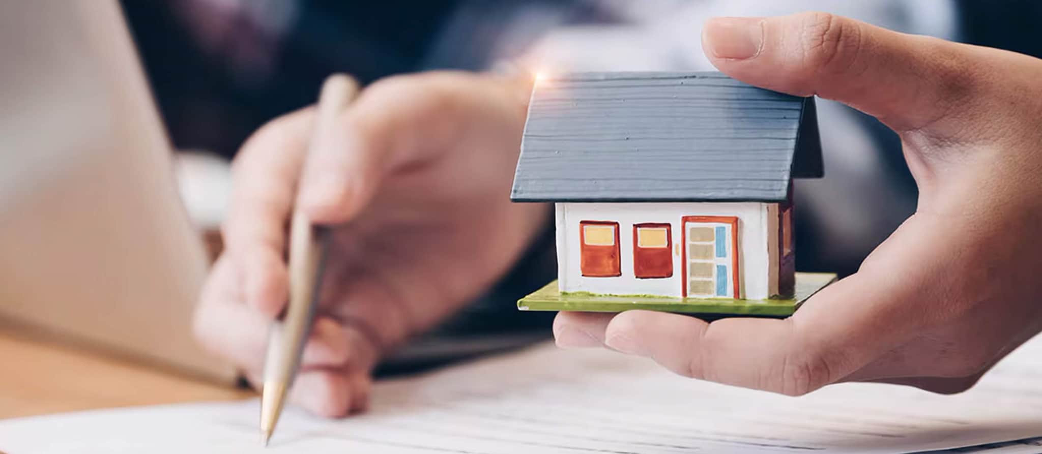 Individual grasping a miniature house, representing the fundamentals of real estate investment.