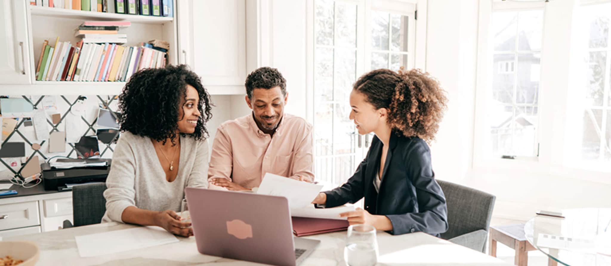 Three individuals engaged in discussion at a kitchen table, with a laptop open, exploring the concept of investing.