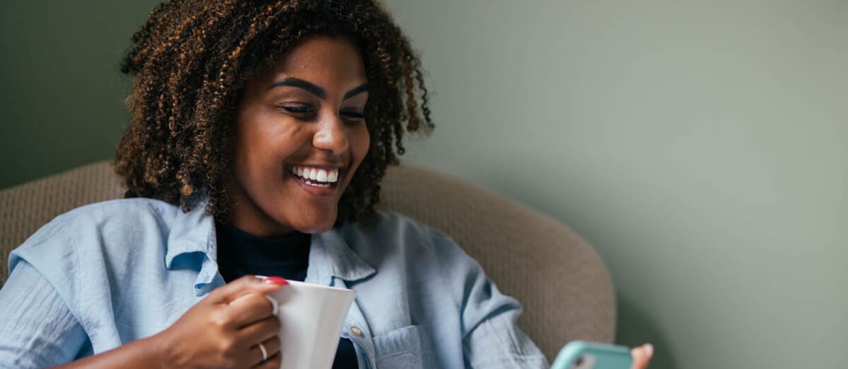 A person with a hot drink smiling while checking their phone.