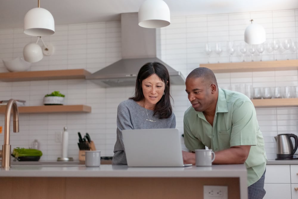 Couple standing in a kitchen and leaning on an island while looking at a laptop