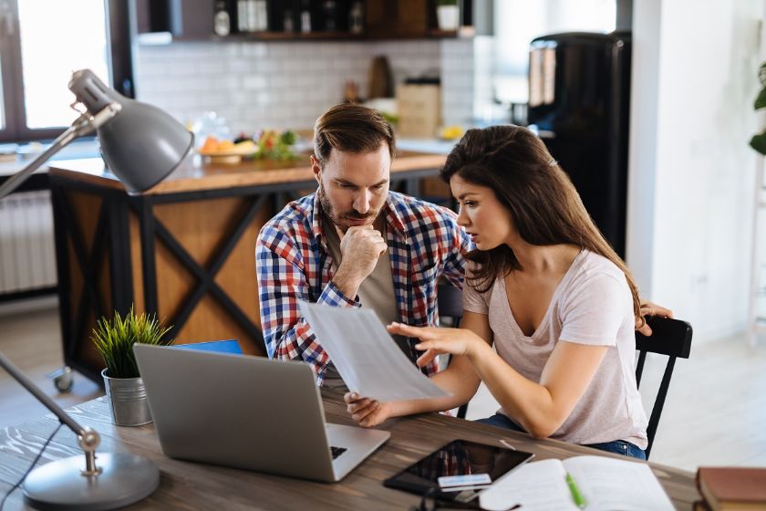 A man and woman collaborate at a table with a laptop, focusing on financial management strategies together.