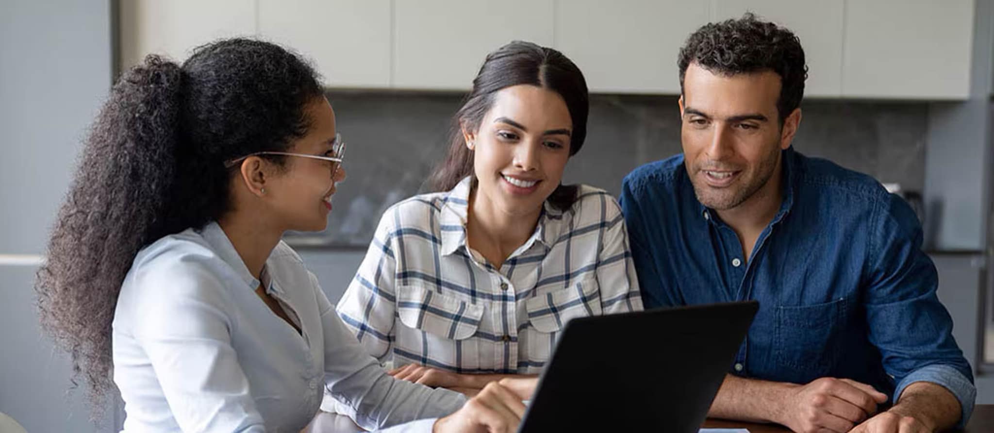 A couple and a young man are gathered around a laptop, discussing the process of opening a checking account.