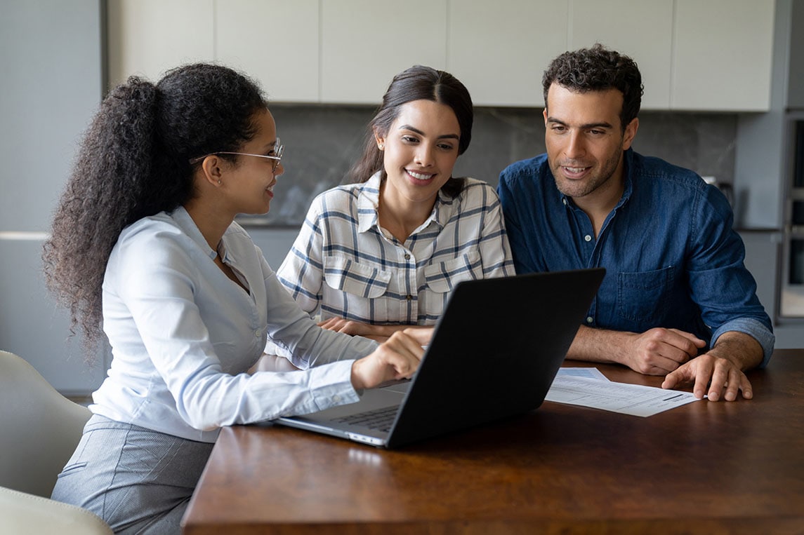 A couple and a young man are gathered around a laptop, discussing the process of opening a checking account.