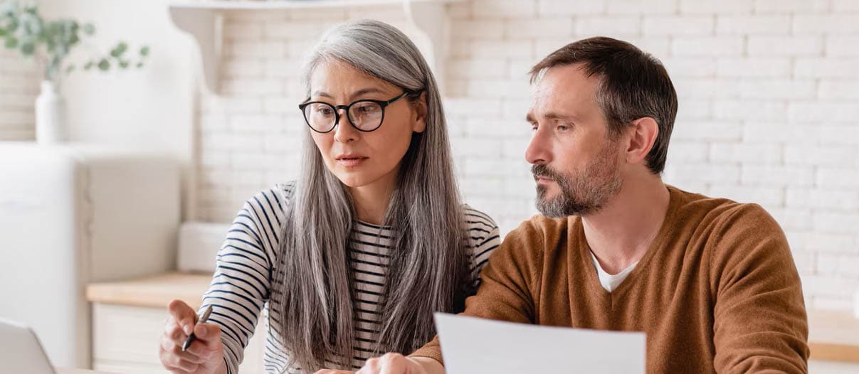 A man and a woman are researching on a laptop how to remove collections from a credit report, using documents and a calculator.
