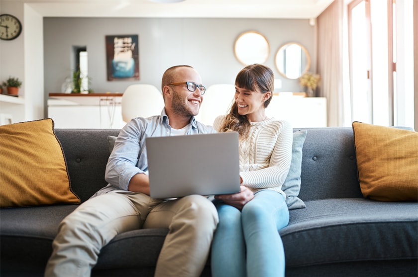A couple checks their credit report online via their laptop while sitting on their couch