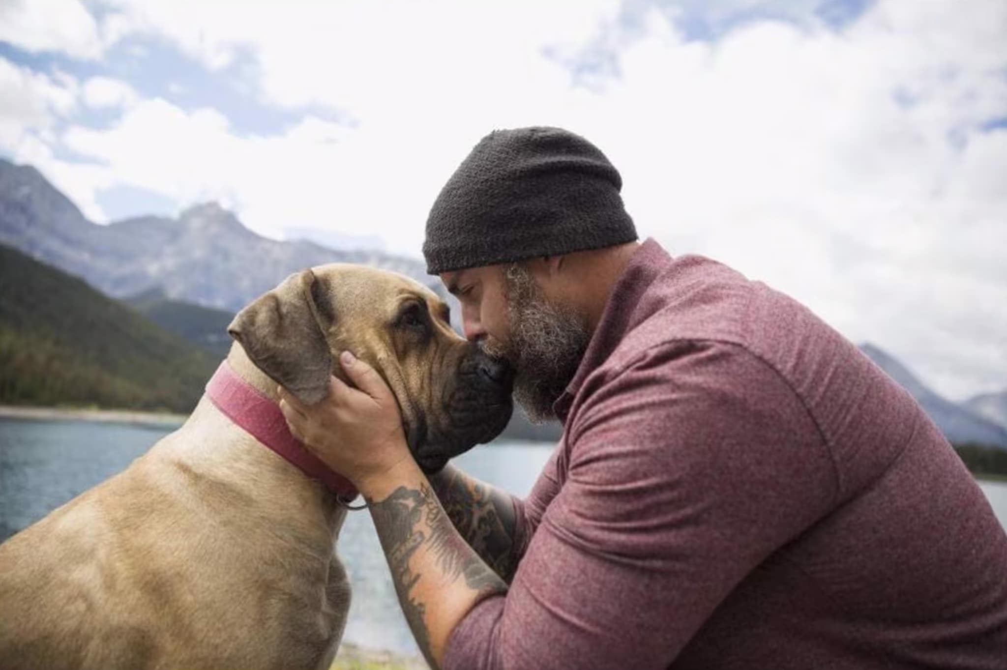 A tattooed man with a beard shares a tender kiss with his dog, highlighting the joy of companionship in his early retirement.