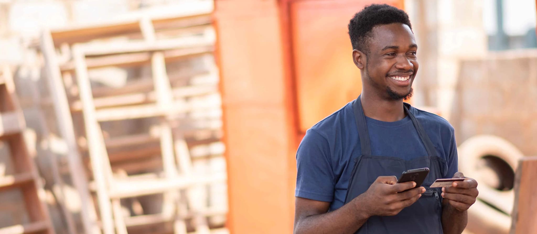 A man in an apron holds a cell phone, symbolizing modern budgeting tips with credit cards.