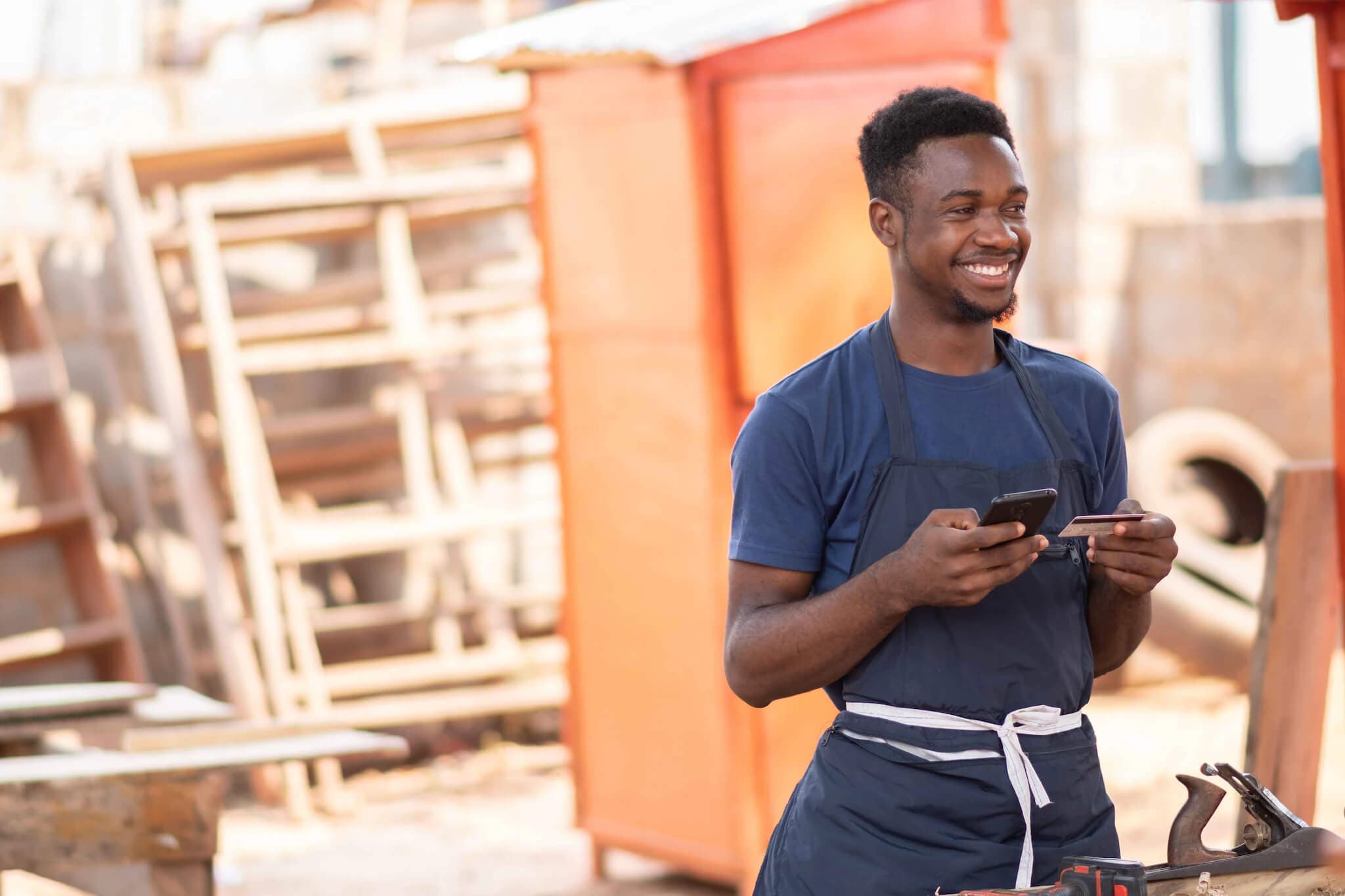 A man in an apron holds a cell phone, symbolizing modern budgeting tips with credit cards.