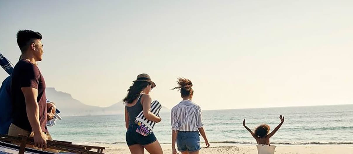 A family strolls along the beach, carrying a suitcase, symbolizing their journey to a well-earned vacation.