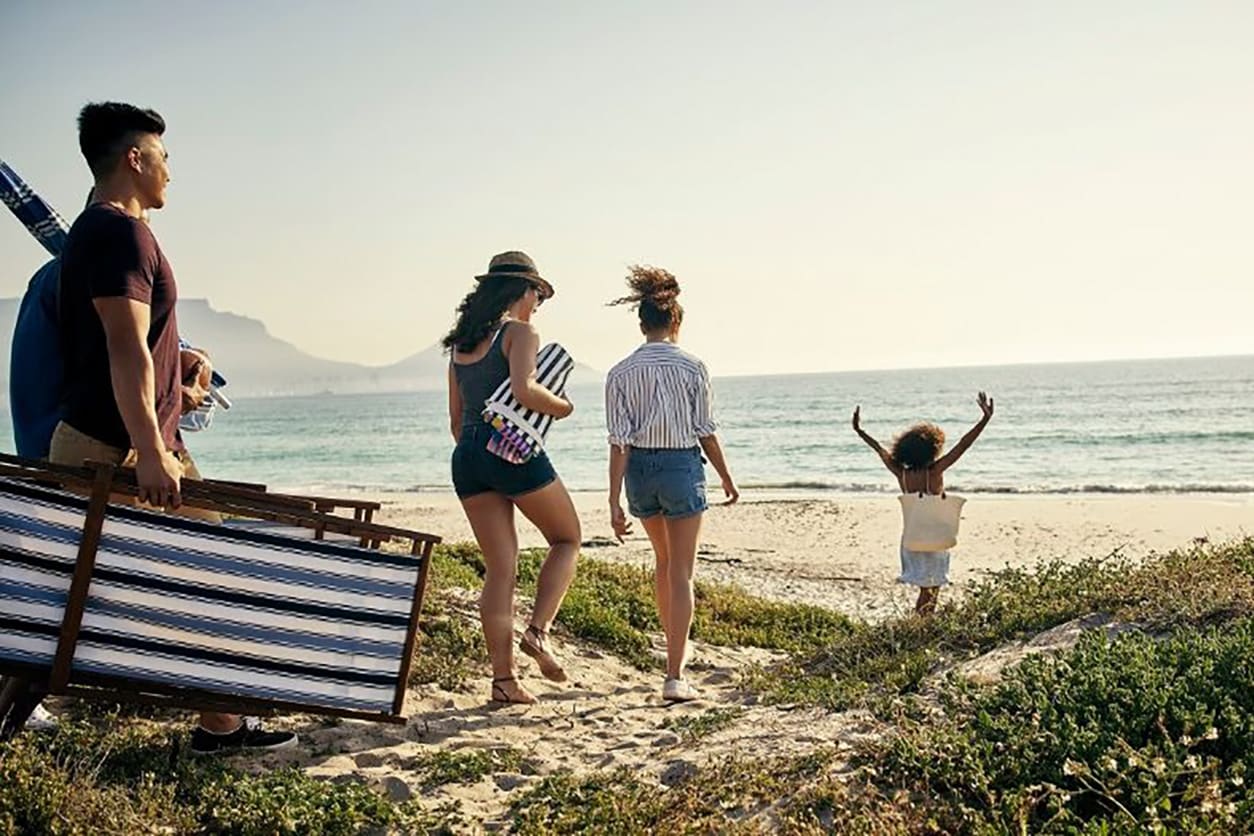 A family strolls along the beach, carrying a suitcase, symbolizing their journey to a well-earned vacation.