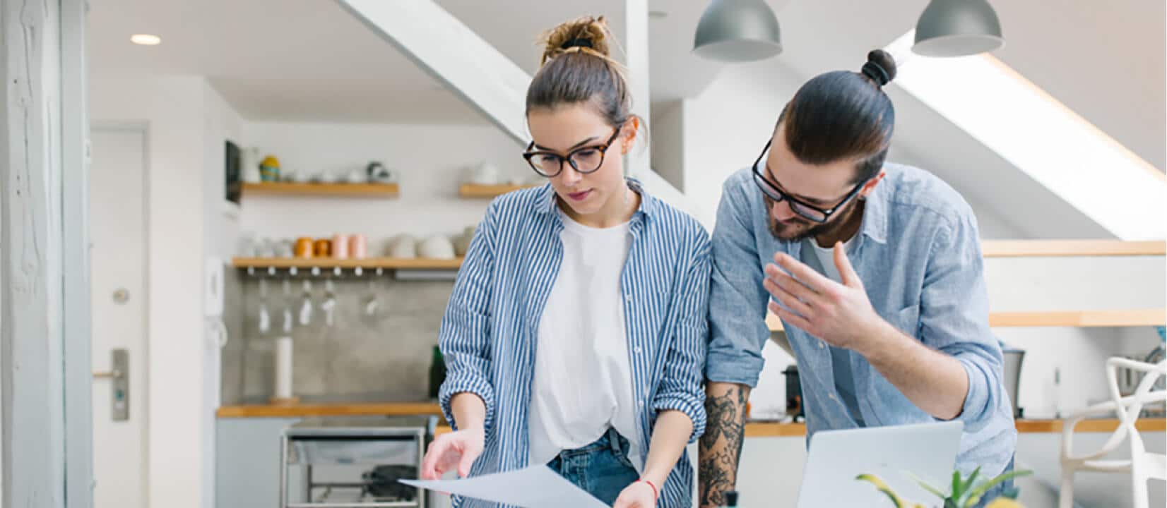 A man and a woman standing over a dining room table while looking over some papers