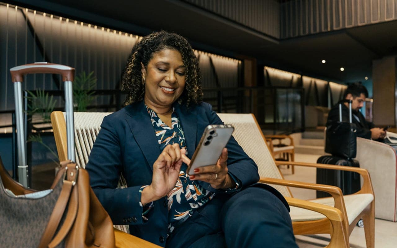 A professional image of a traveler at an airport, reviewing their flight itinerary on a smartphone.