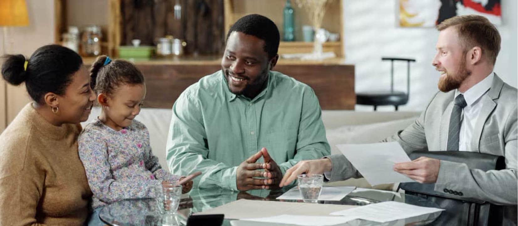 Two parents and their child are sitting with a bank employee, discussing how to open a savings account for the child