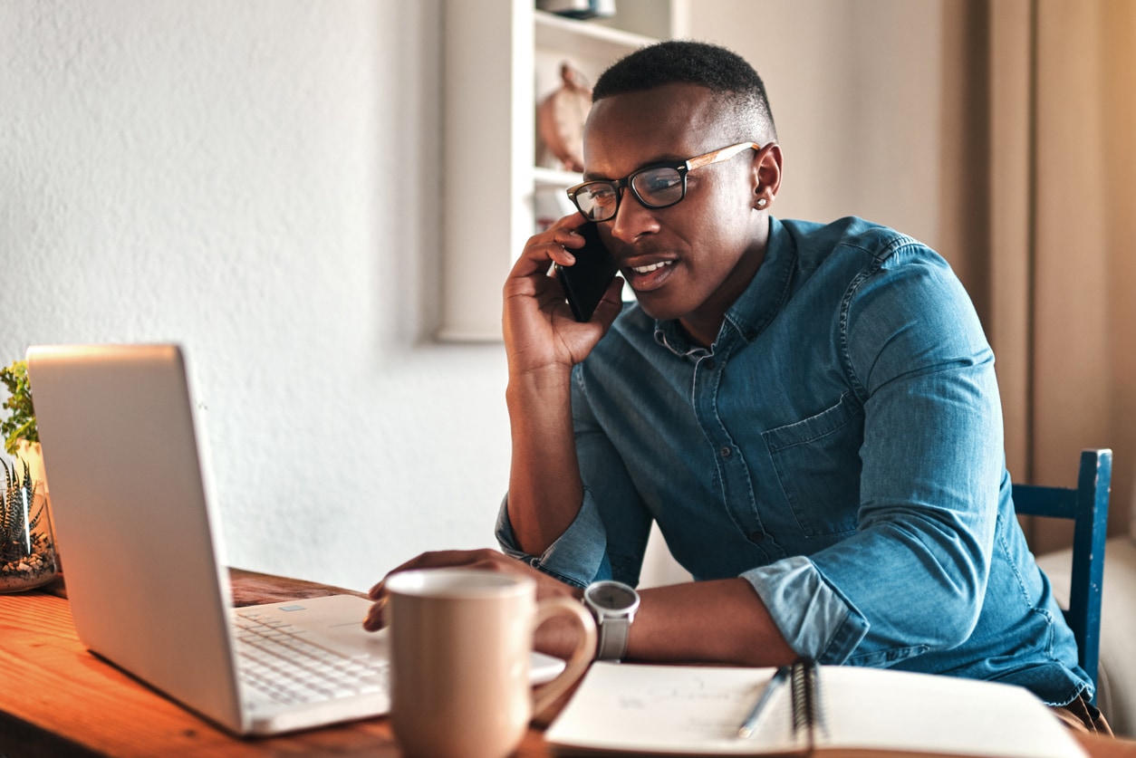 A man talking on the phone while typing on his laptop