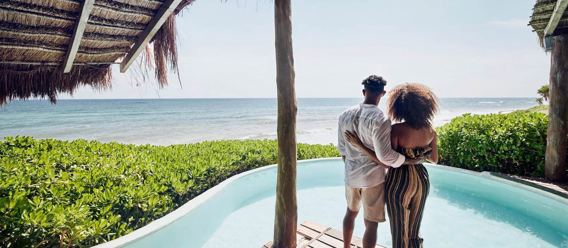 Couple standing on a deck overlooking a pool and the ocean in a tropical place