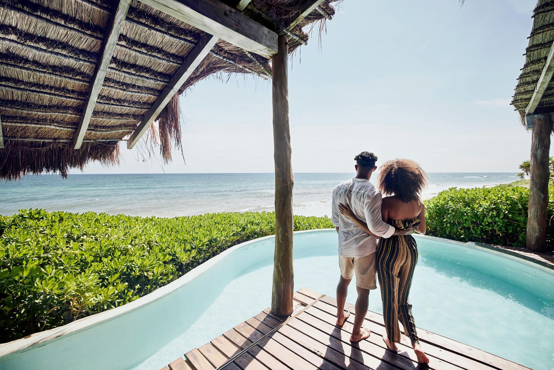 Couple standing on a deck overlooking a pool and the ocean in a tropical place