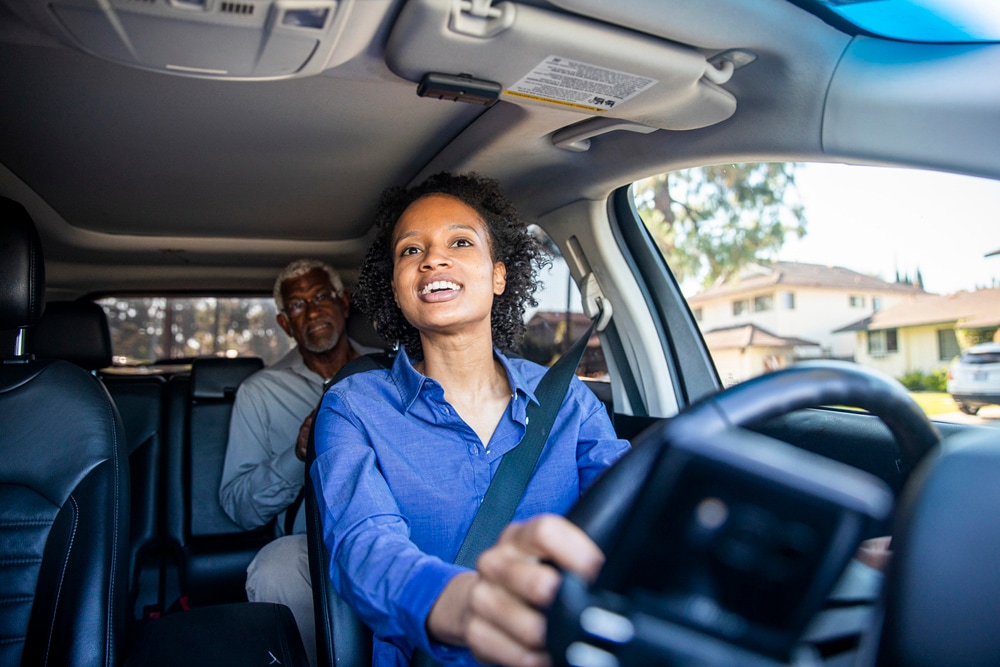 A woman driving a car, smiling at a man in the backseat