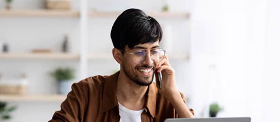 A boy talking on the phone while working on a laptop.