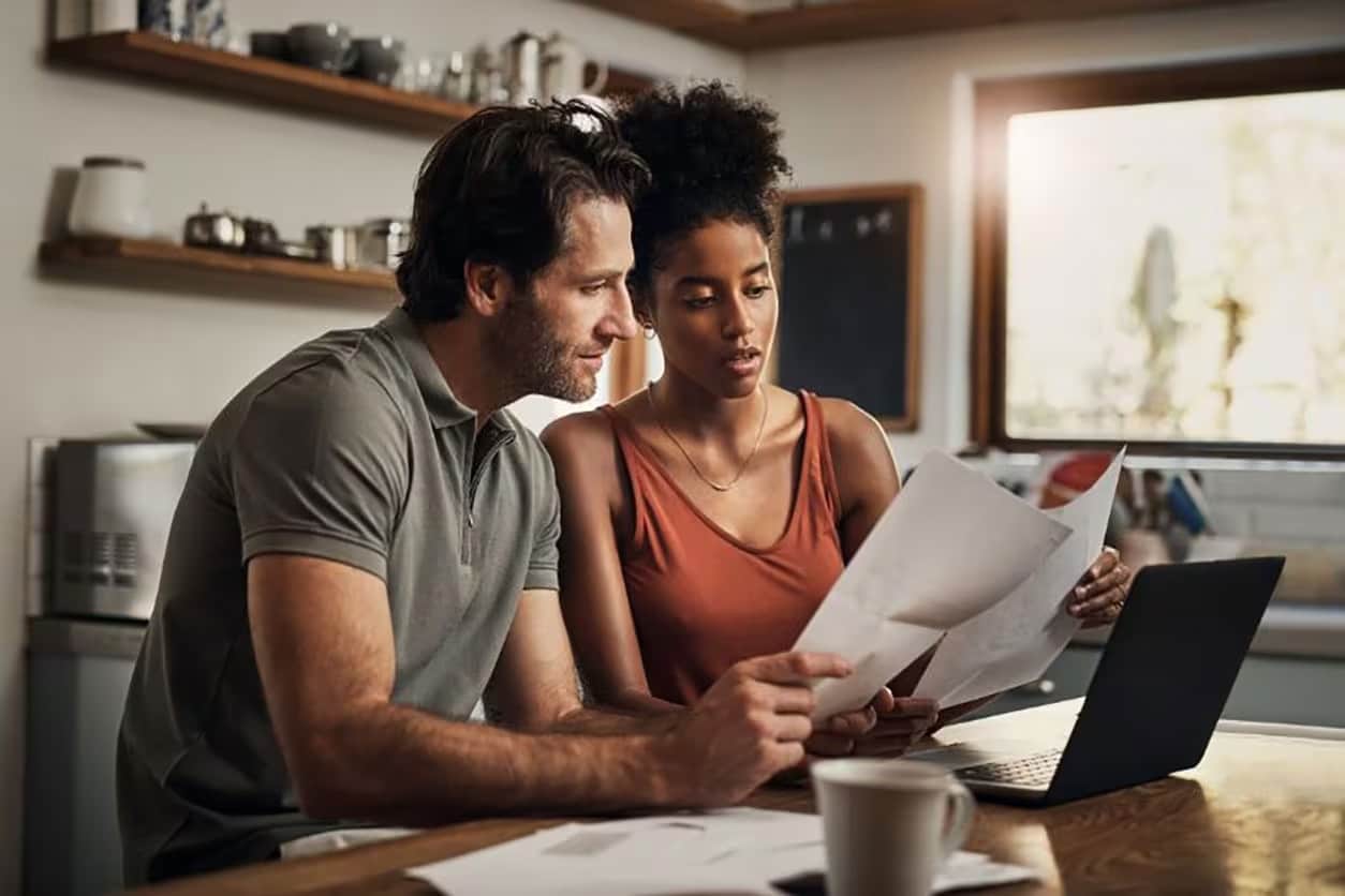 A man and woman review paperwork together in a kitchen, discussing credit card payment strategies.
