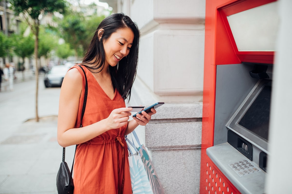 A professional image of a person using a mobile banking app to deposit a check, with an ATM in the background.