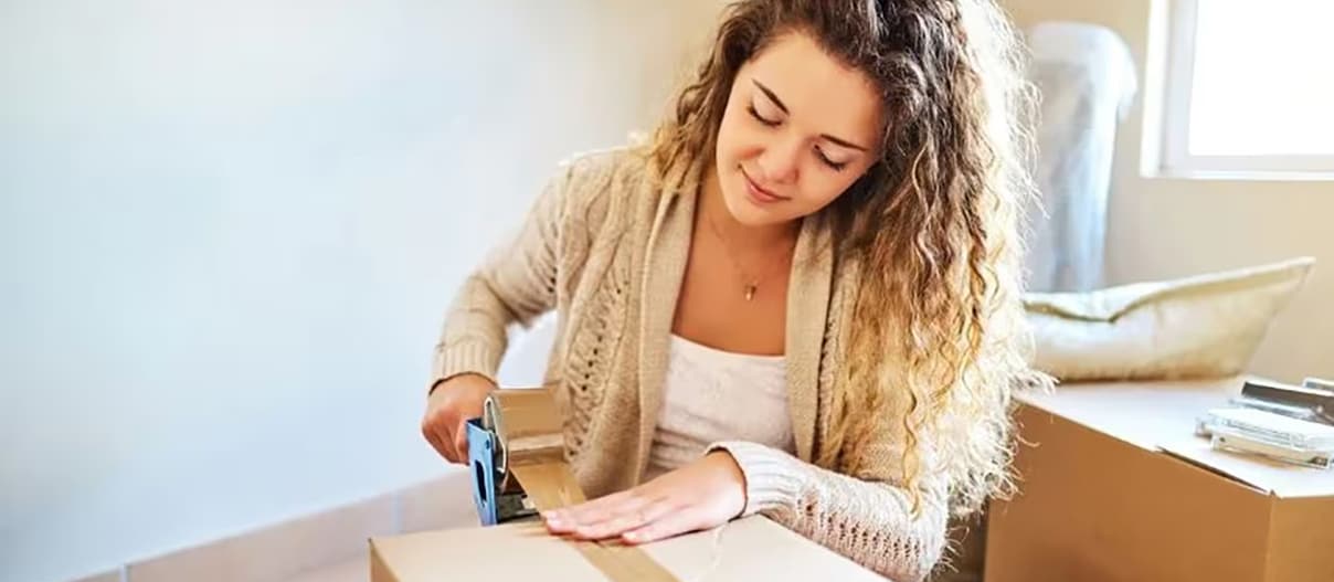 Woman is tapping a moving box close with a tape on a floor