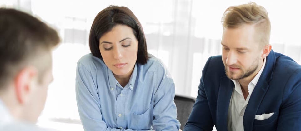 Three people sitting at a table looking over a spreadsheet.