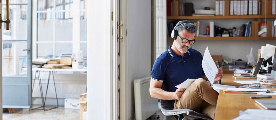 A man sitting on a chair and reading documents while wearing headphones.