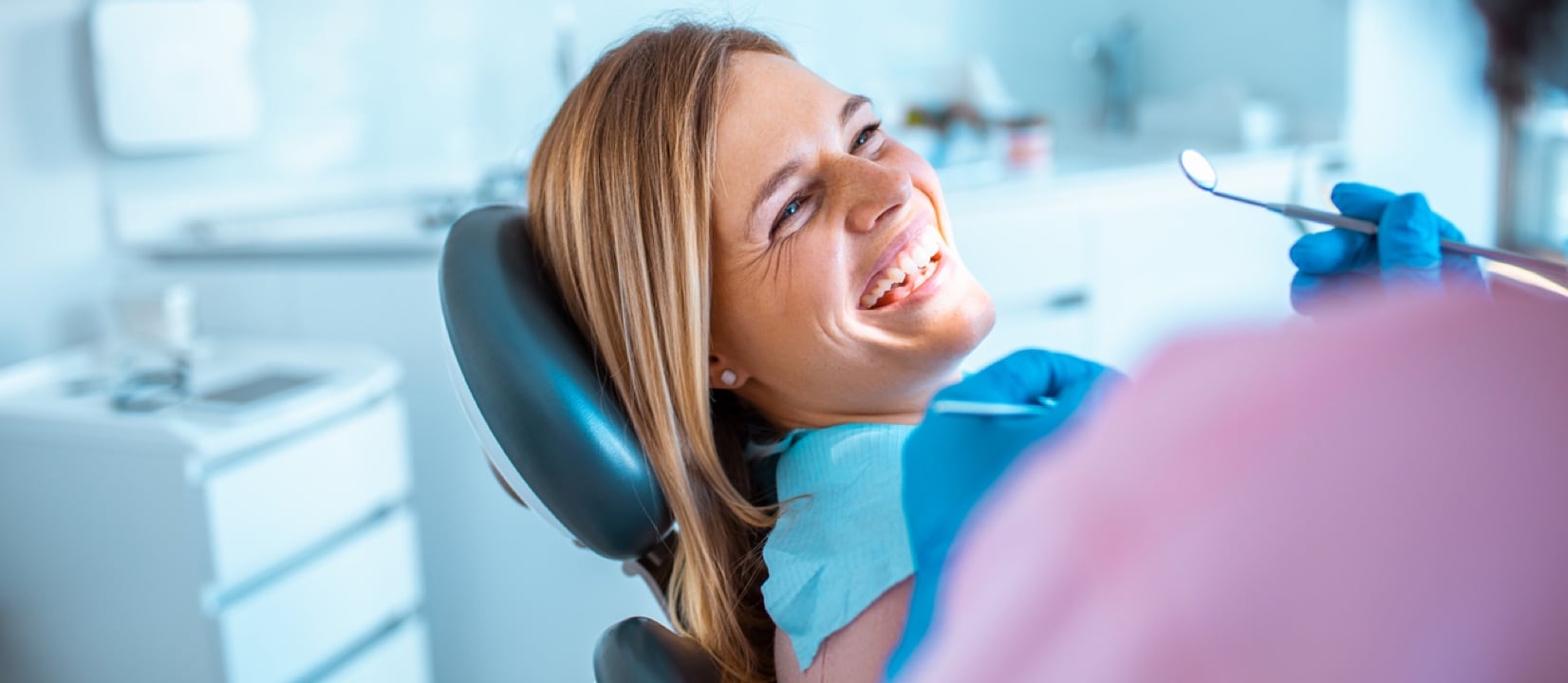 A woman at a dental clinic talking to the doctor and smiling.