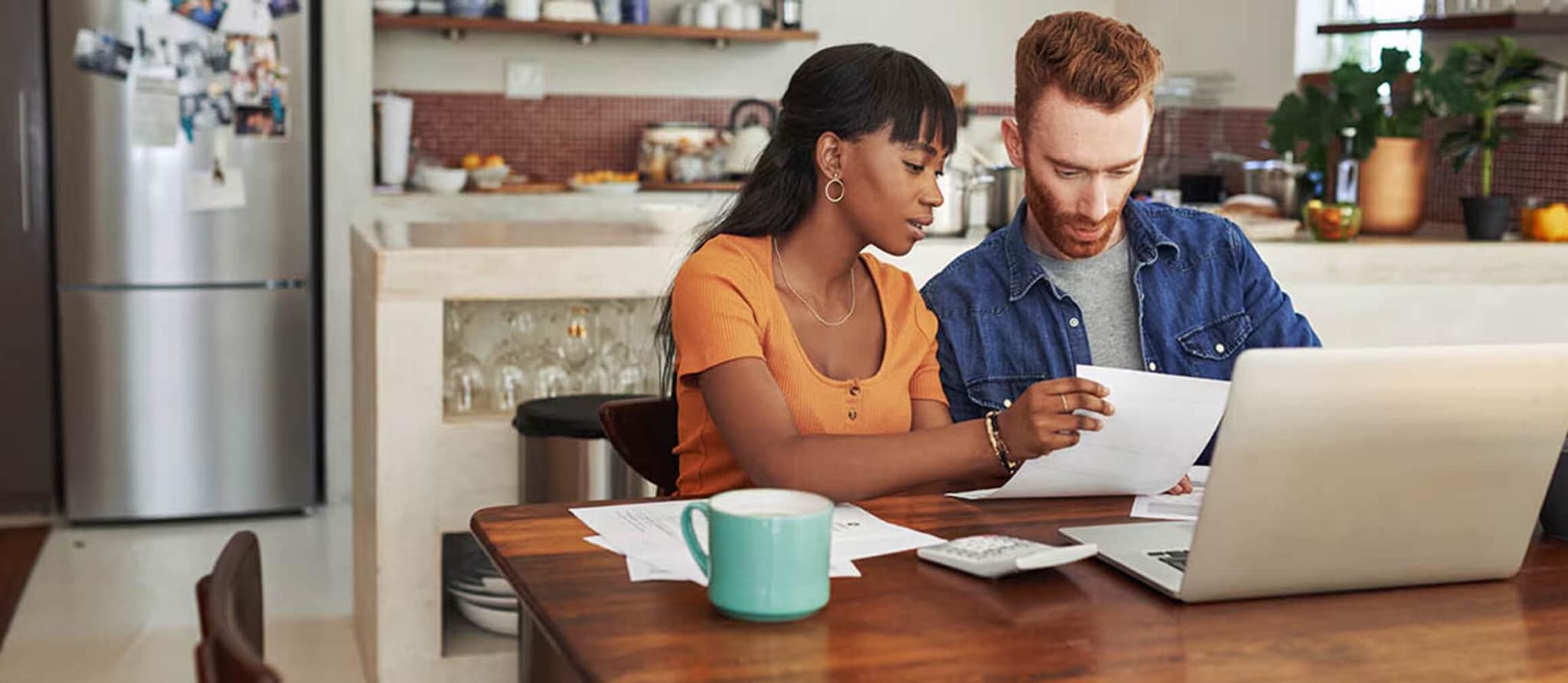 A man and woman seated at a table, engaged with a laptop, discussing pending transactions and their implications.