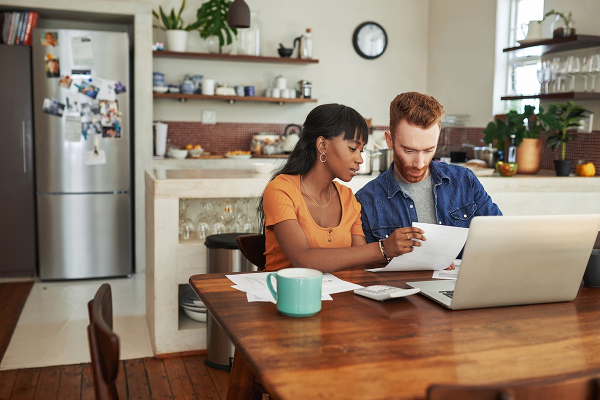 A man and woman seated at a table, engaged with a laptop, discussing pending transactions and their implications.