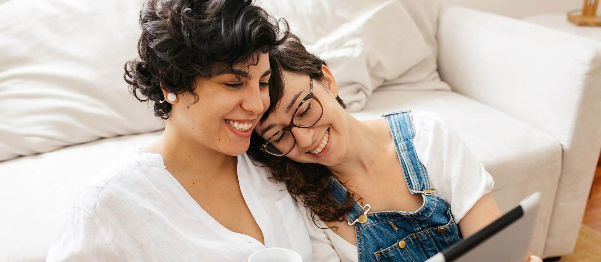 Two women seated on a couch, engaged with a tablet, exploring personal finance resources for LGBTQ+ Americans.