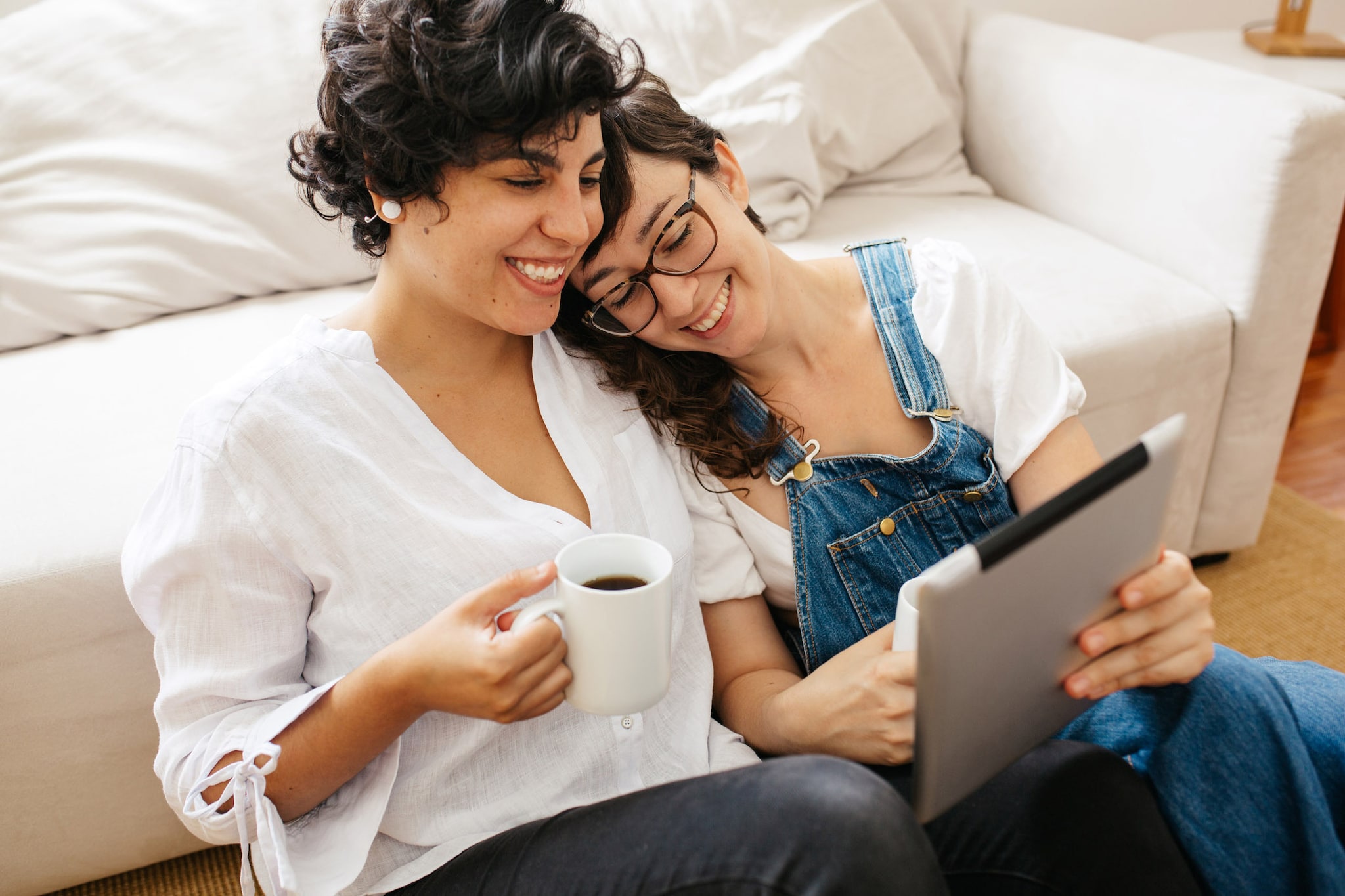 Two women seated on a couch, engaged with a tablet, exploring personal finance resources for LGBTQ+ Americans.