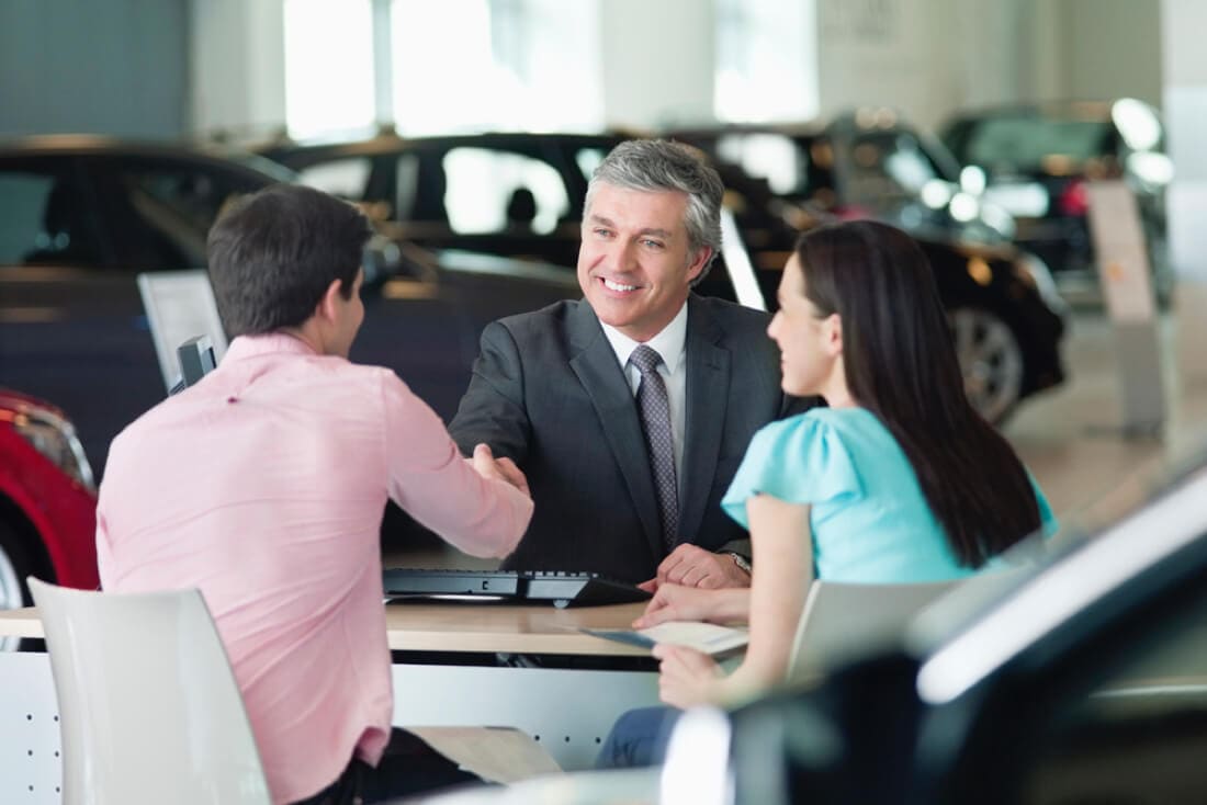 A couple shaking hands with a professional at a car dealership.