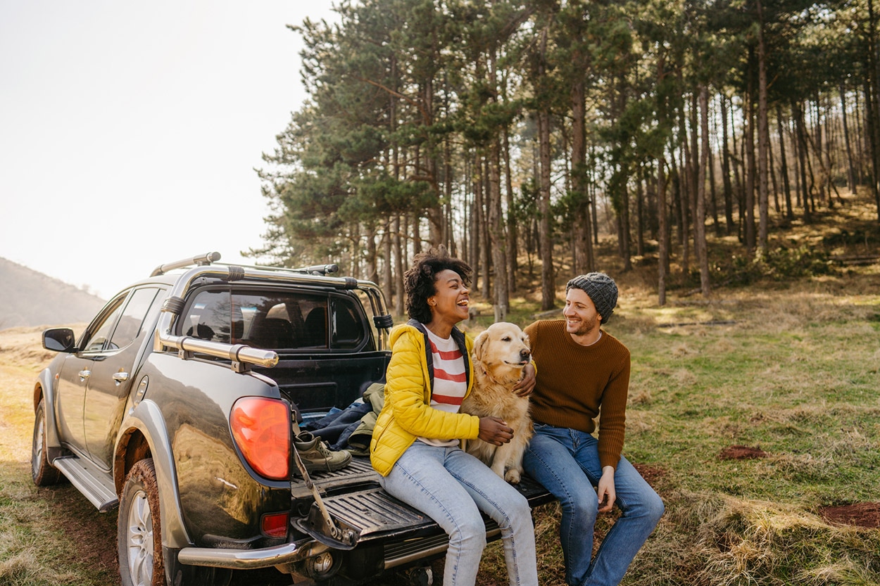 Two people enjoying a conversation while sitting on the back of a pickup truck with a dog between them