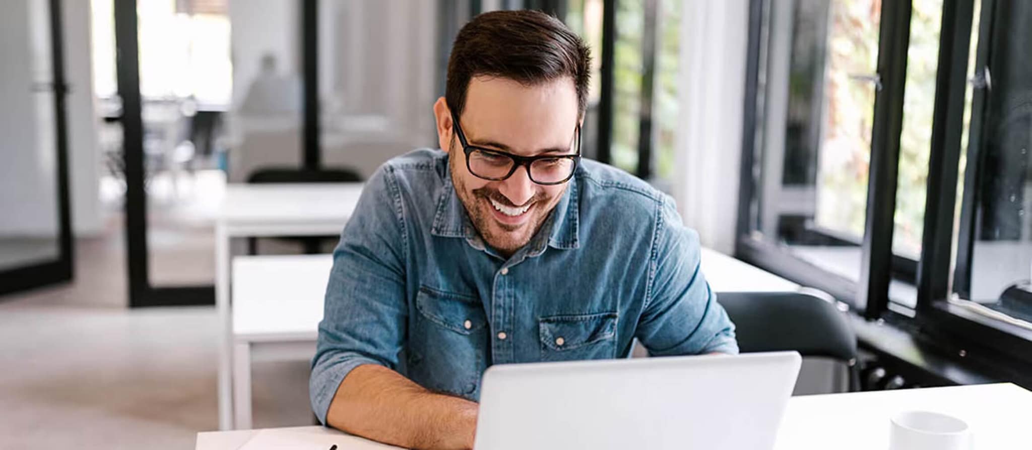 A man in glasses smiles while using a laptop, symbolizing strategic investment planning and portfolio diversification.