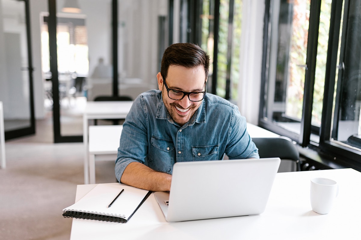 A man in glasses smiles while using a laptop, symbolizing strategic investment planning and portfolio diversification.