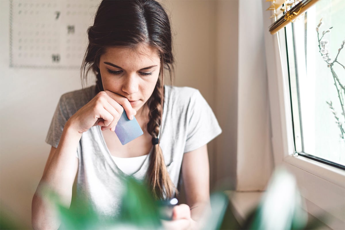 A woman sits holding her credit card while looking at her phone.