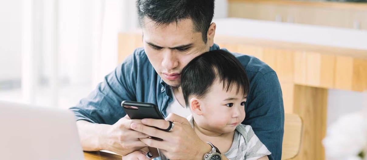 A man and a baby engage with a smartphone at home, highlighting the importance of retirement funding for future security.