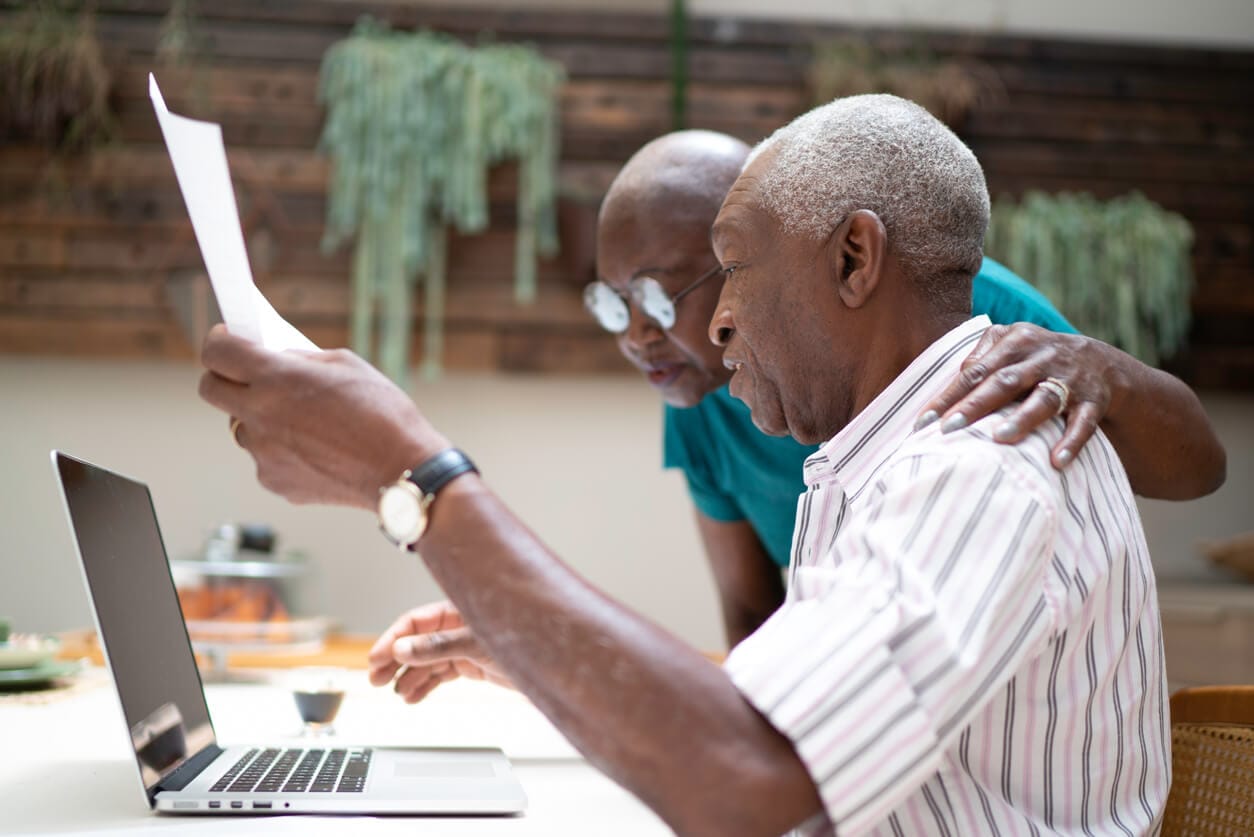 An elderly couple analyzing a document on a laptop, engaged in a discussion about retirement investment choices.