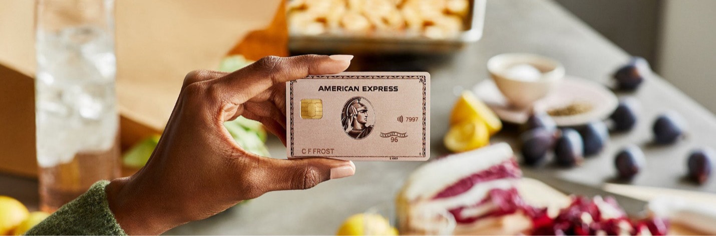 Rose Gold American Credit Card in a hand of a person in front of a table full of food.