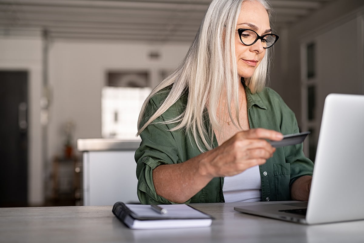 A woman in glasses is working on her laptop, highlighting the importance of credit cards and their routing numbers.