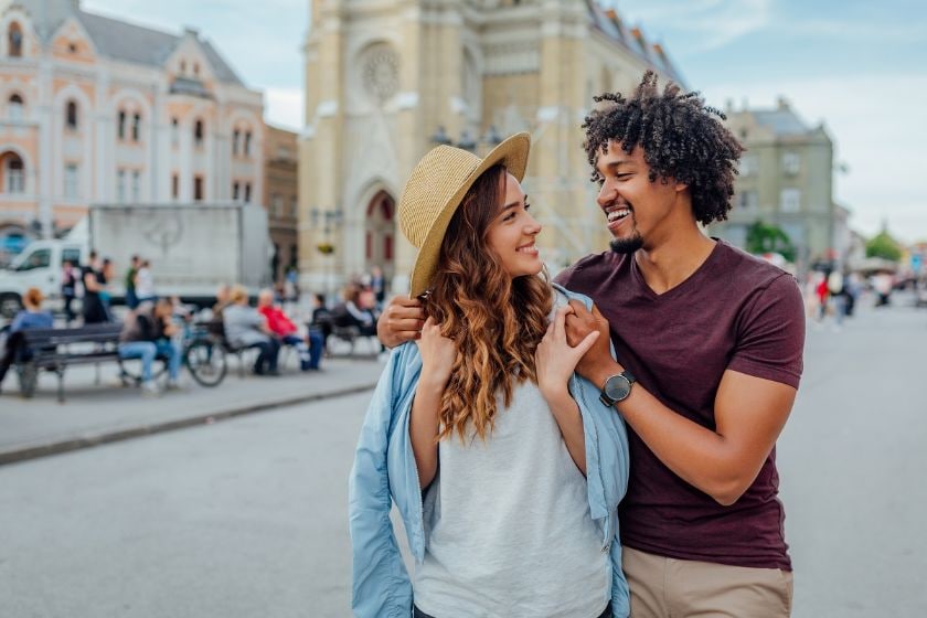 A young couple smiles at each other in the city, embodying joy and connection while exploring travel opportunities together.