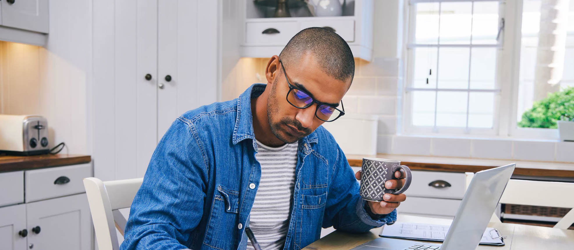 A man is noting down how to stop spending money while enjoying a cup of coffee.