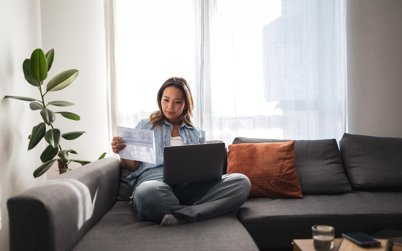 A professional image of a person reviewing financial documents at home, with a laptop and a cup of coffee on the table.