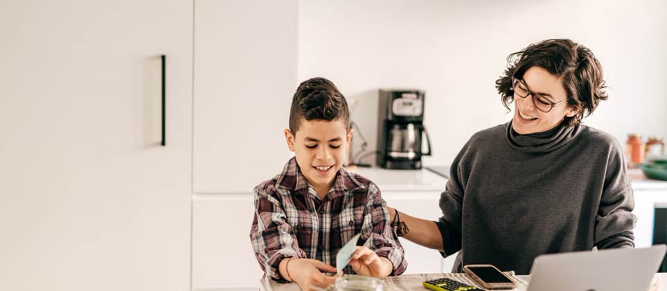 A parent is teaching her child about money while they sit at the dining table.